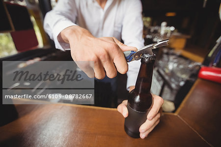 Close-up of bartender opening a beer bottle at bar counter