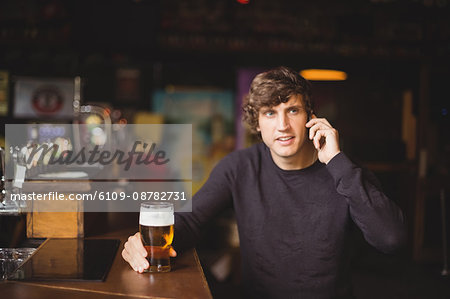 Man talking on mobile phone in bar with glass of beer in hand