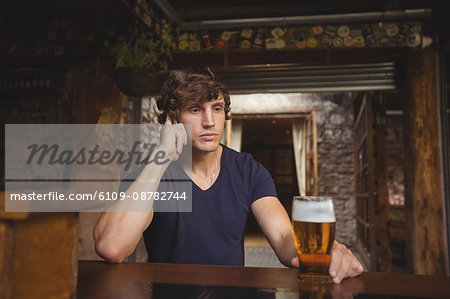Man talking on mobile phone in bar with glass of beer in hand