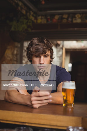 Man using mobile phone with beer glass on table in bar