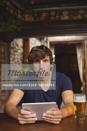 Portrait of man using digital tablet with beer glass on table in bar