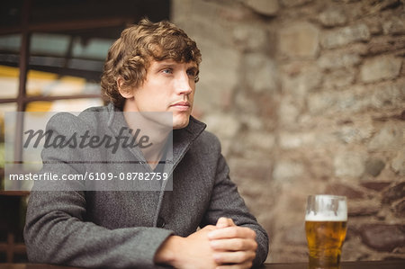 Thoughtful man sitting in bar with glass of beer on table