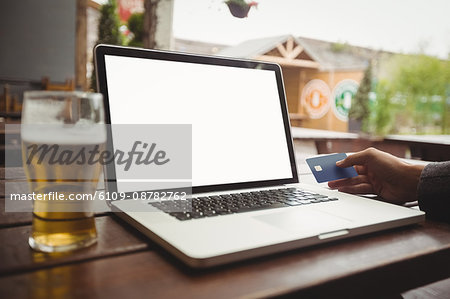 Man doing online shopping with credit card on laptop in bar