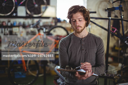 Mechanic writing on clipboard in bicycle shop