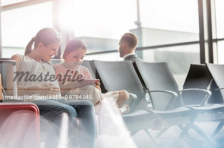 Pregnant mother and daughter using digital tablet in airport departure area