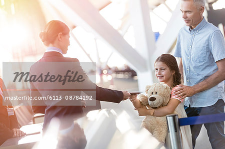 Flight attendant checking ticket of girl with teddy bear in airport