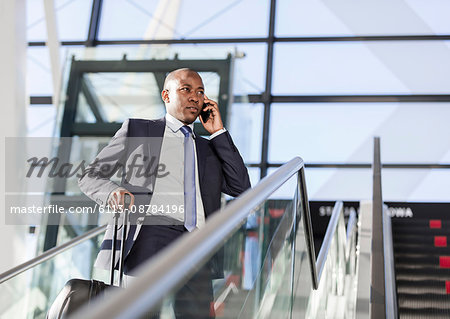 Businessman talking on cell phone on airport escalator