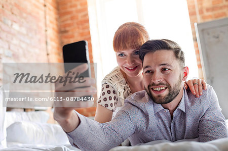 Couple laying on bed taking selfie with camera phone