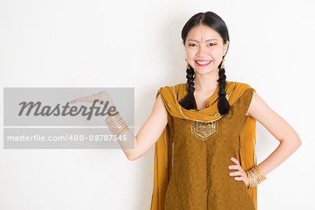 Portrait of young mixed race Indian Chinese female in traditional punjabi dress hand holding somethings, standing on plain white background.