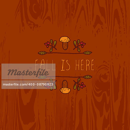 Hand-sketched typographic element with mushroom, berries and text on wooden background. Fall is here