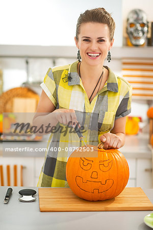 Frightful Treats on the way. happy young woman in the Halloween decorated kitchen carving a big orange pumpkin Jack-O-Lantern