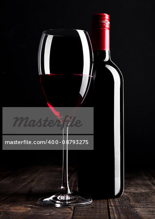 Red wine bottle and glass on wooden table black background