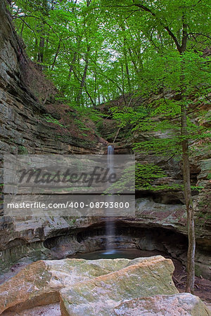 Glowing like a laser beam, the St. Louis Canyon waterfall in Starved Rock State Park,tumbles to the ground. Limestone rocks and trees stand guard over the waterfall.