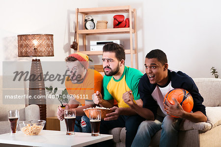 Picture of friends watching football game on TV while spending their weekends at home with alcohol drinks and pop corn. Football concept.