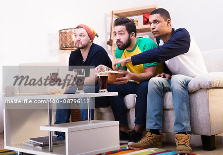 Low view of happy friends watching football game on TV, commenting all moments emotionally and drinking beer with pop corn.