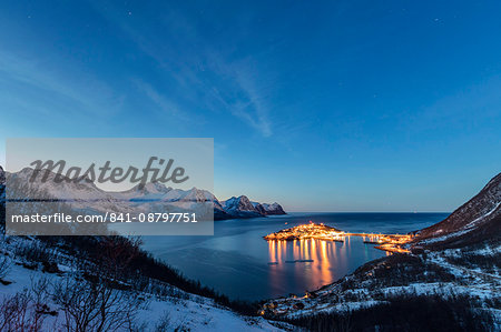 Lights on the typical fishing village framed by the frozen sea at dusk, Husoy, Fjordbotn, Senja, Troms County, Norway, Scandinavia, Europe