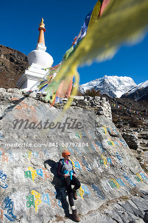 A woman trekking in the Langtang valley stops near a colorful Mani Stone wall below a Stupa decorated with Buddhist prayer flags, Langtang Region, Himalayas, Nepal, Asia