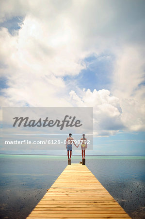 Young couple hold hands while balancing on an ocean pier.