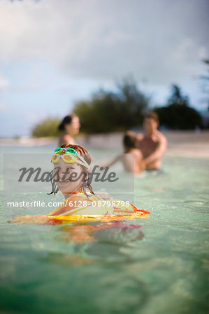 Portrait of a smiling young girl swimming with her family at a tropical beach.