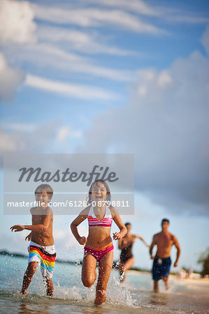 Happy family splashing in shallow water at a tropical beach.