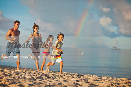 Happy family running on the sand at a tropical beach.