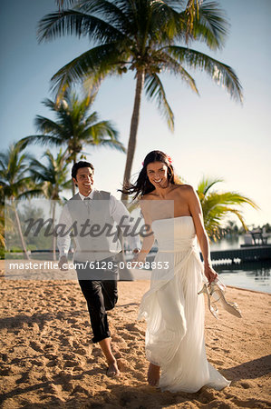 Playful young newlywed couple walking along a beach after their wedding.