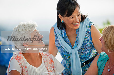 Two mature female friends out to lunch share a laugh with an acquaintance who has come to say hello.