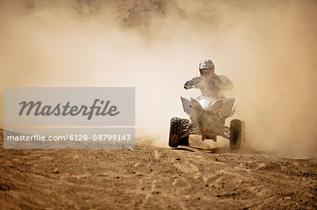 Quadbiker rides through dusty dirt road.