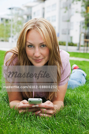 Portrait of smiling woman lying on grass and using mobile phone