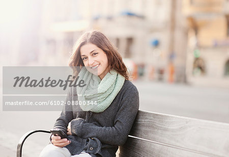 Portrait of young woman sitting on bench using phone