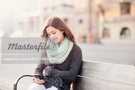 Young woman sitting on bench using phone