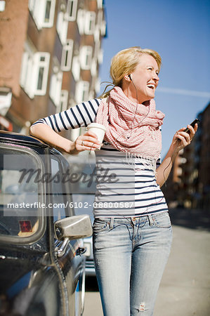 Woman using a mobile phone by a car, Sweden.