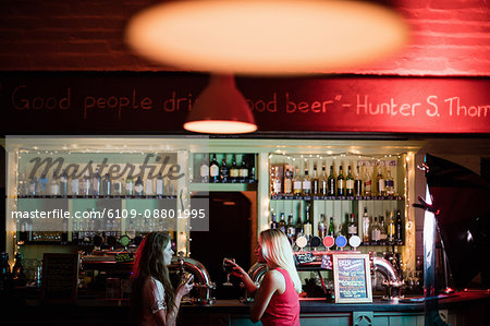 Women interacting while having a glasses of wine at counter in bar
