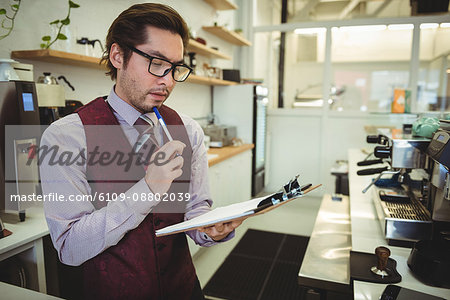 Thoughtful man looking at clipboard in coffee shop