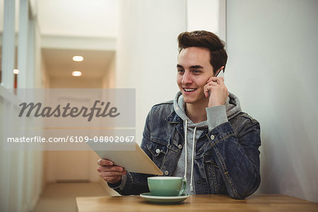 Man talking on mobile phone while holding digital tablet in coffee shop