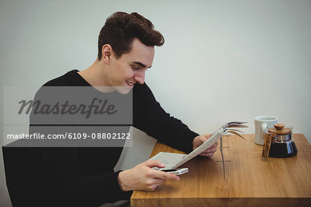Man with mobile phone reading newspaper in coffee shop