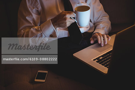 Mid section of businessman using laptop while having coffee at home