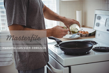 Mid section of man pouring olive oil into the frying pan in the kitchen at home