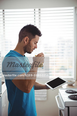 Man using his digital tablet while having glass of juice in kitchen at home