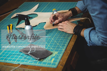 Mid-section of craftswoman working on a piece of leather in workshop