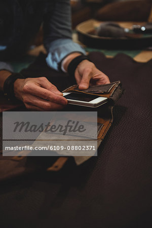 Craftswoman preparing leather cover for mobile phone in workshop