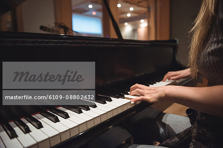 Mid section of woman playing a piano in music studio
