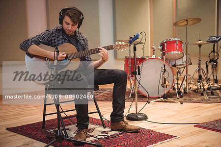 Man sitting on chair and playing a guitar in music studio