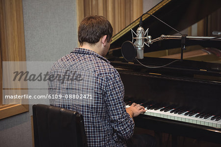 Rear view of man playing a piano in music studio
