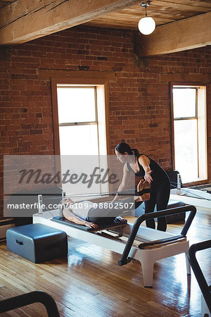 Trainer helping a woman while practicing pilates in fitness studio