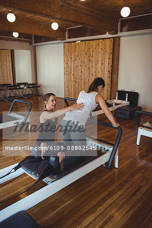 Trainer helping a woman while practicing pilates in fitness studio