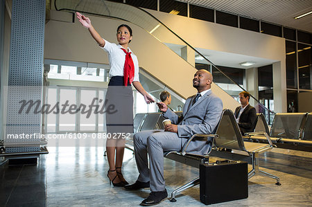 Female staff showing directions to businessman at airport terminal Female staff showing directions to businessman at airport terminal