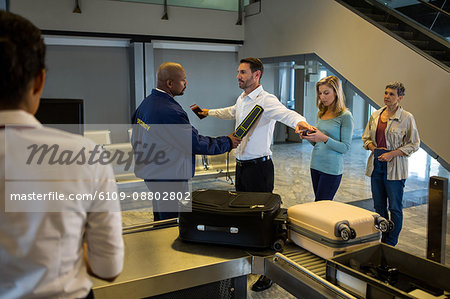 Security guard frisk passengers standing in queue at airport terminal