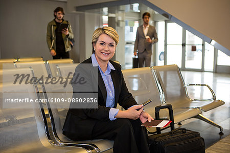 Businesswoman with passport, boarding pass and luggage sitting in waiting area at airport terminal