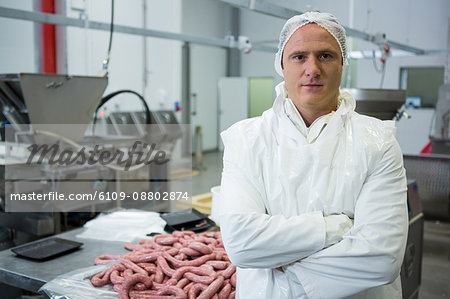 Portrait of male butcher standing with arms crossed at meat factory